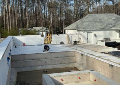 Pool shell under construction at the Cahaba Living project, woodland behind