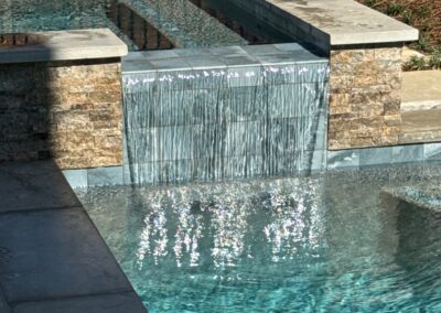Raised stone spa with a sheet waterfall spilling into the finished pool at Greystone Dream